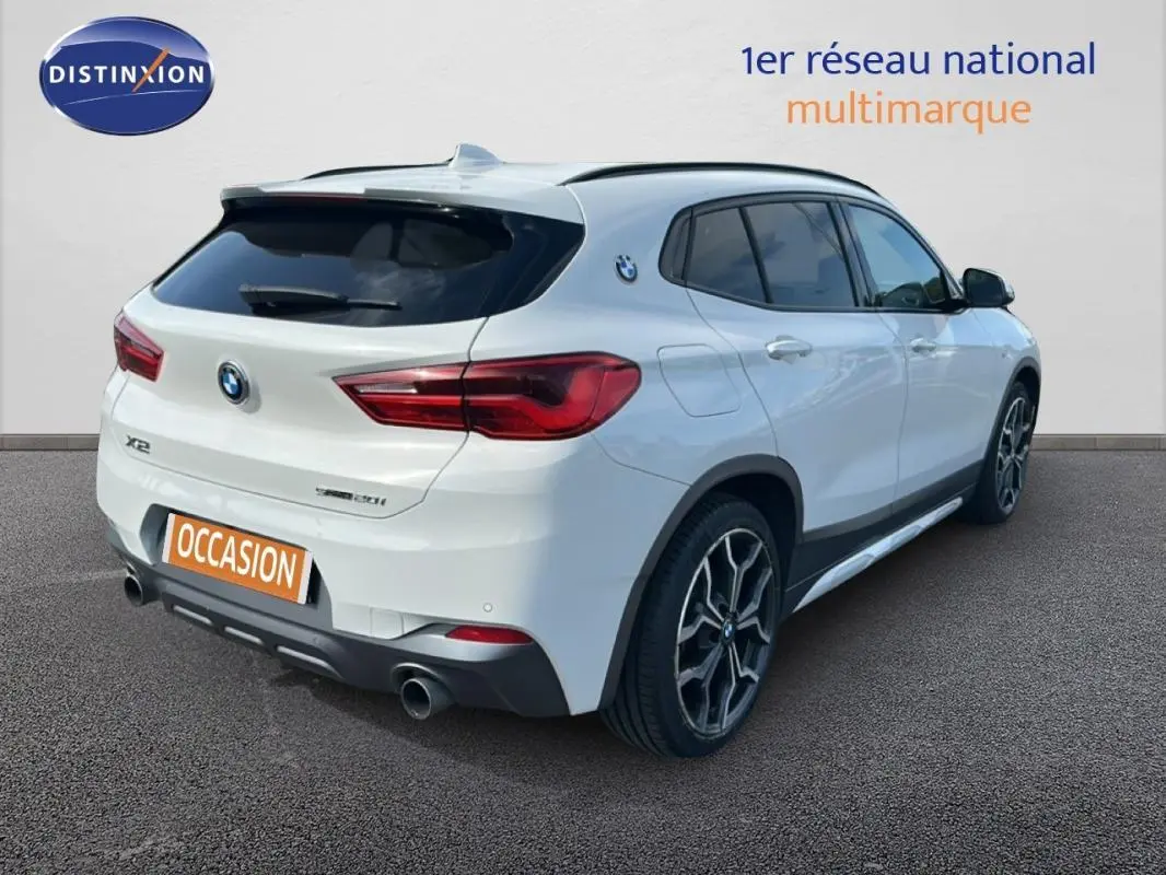 Vue 3/4 arrière droite d’un BMW X2 blanc avec jantes alliage 19 pouces et double sortie d’échappement.
