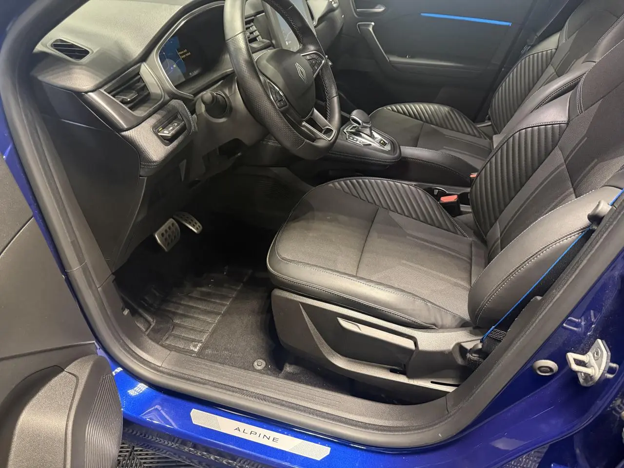 Intérieur côté conducteur de la Renault Symbioz bleu, sièges noirs avec surpiqûres bleues et seuil de porte Alpine visible.