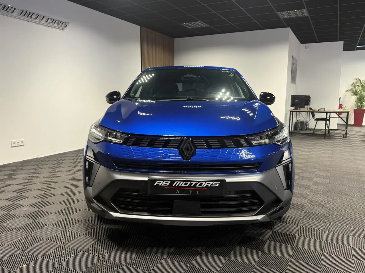 Vue de face d'une Renault SYMBIOZ 1.6 E-Tech Hybride bleu Iron avec calandre noire et détails gris mat en showroom.