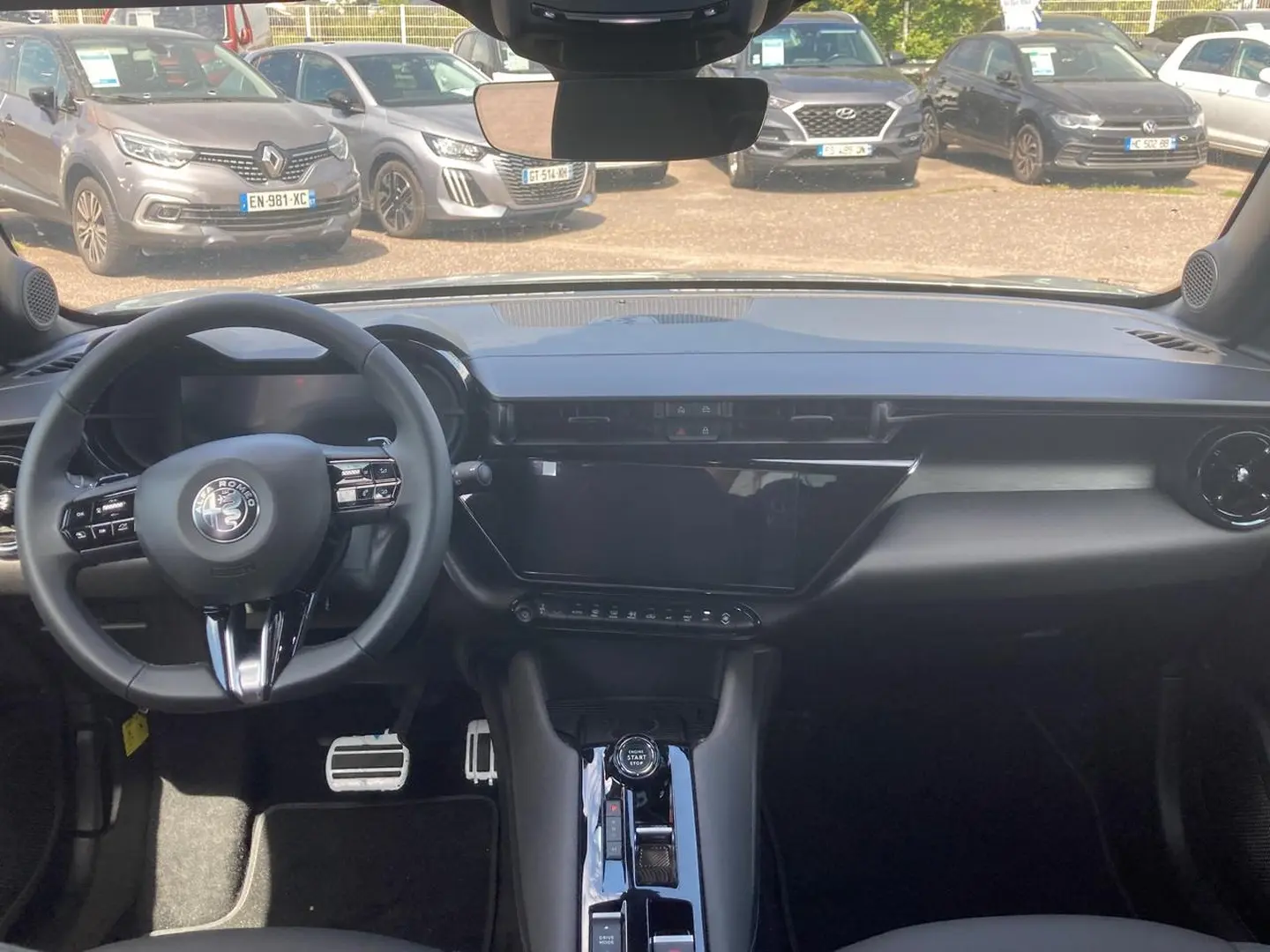 Vue intérieure avant de l'Alfa Romeo Junior 1.2 hybride 2026, tableau de bord noir avec écran tactile et volant multifonction.