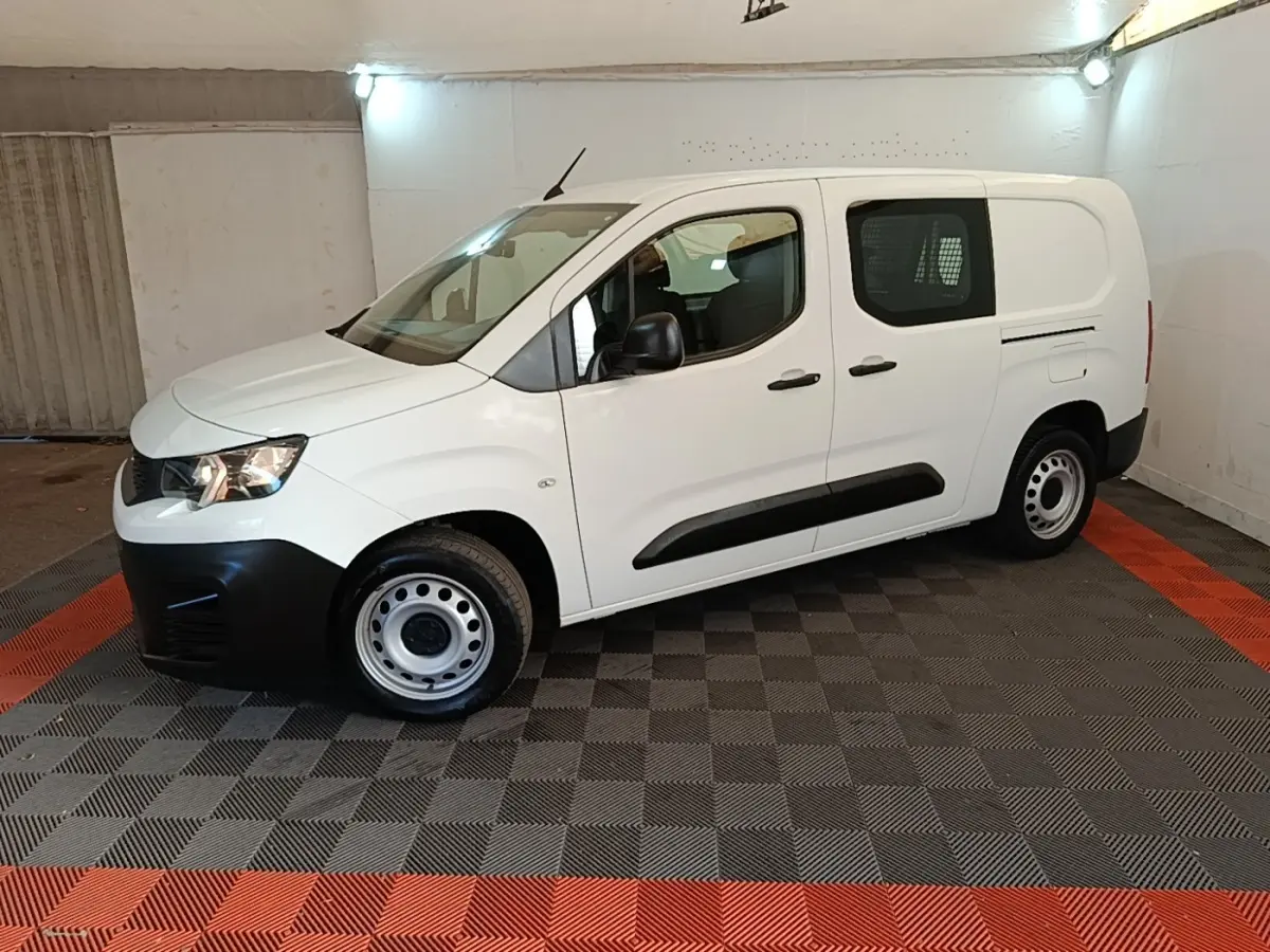 Peugeot Partner blanc en vue de profil côté gauche, avec cloison grillagée visible à l'arrière.