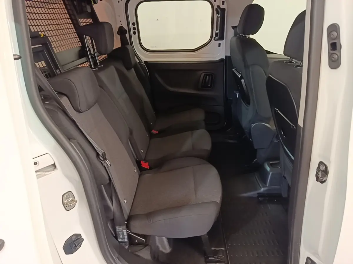 Vue intérieure côté droit sur la banquette arrière noire du Peugeot Partner blanc avec cloison grillagée visible.