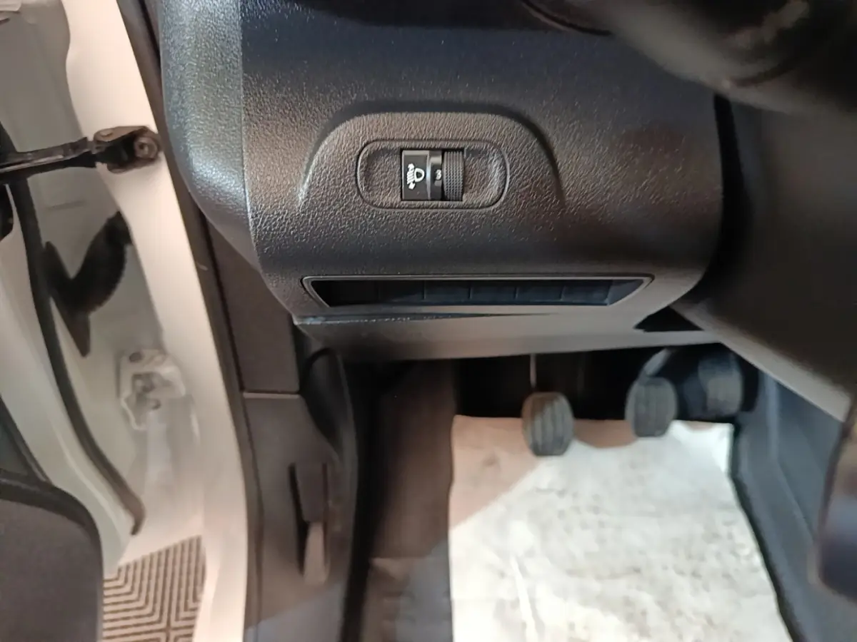 Vue intérieure côté conducteur du Peugeot Partner blanc 2020, montrant les pédales et le réglage des phares.