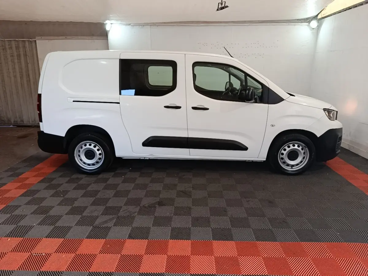 Vue de profil côté gauche d'un Peugeot Partner blanc, utilitaire avec vitres avant et arrière et jantes acier.