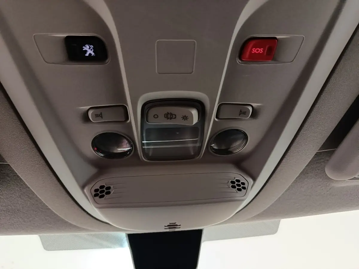 Vue en contre-plongée du panneau de commande intérieur au plafond du Peugeot Partner blanc, avec bouton SOS rouge et éclairage.