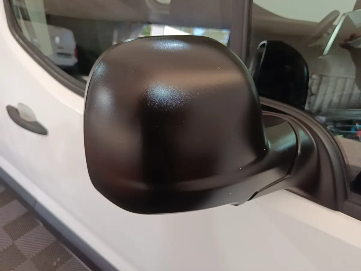 Rétroviseur noir en gros plan sur le côté gauche d’un Peugeot Partner blanc, vue rapprochée de la porte avant.