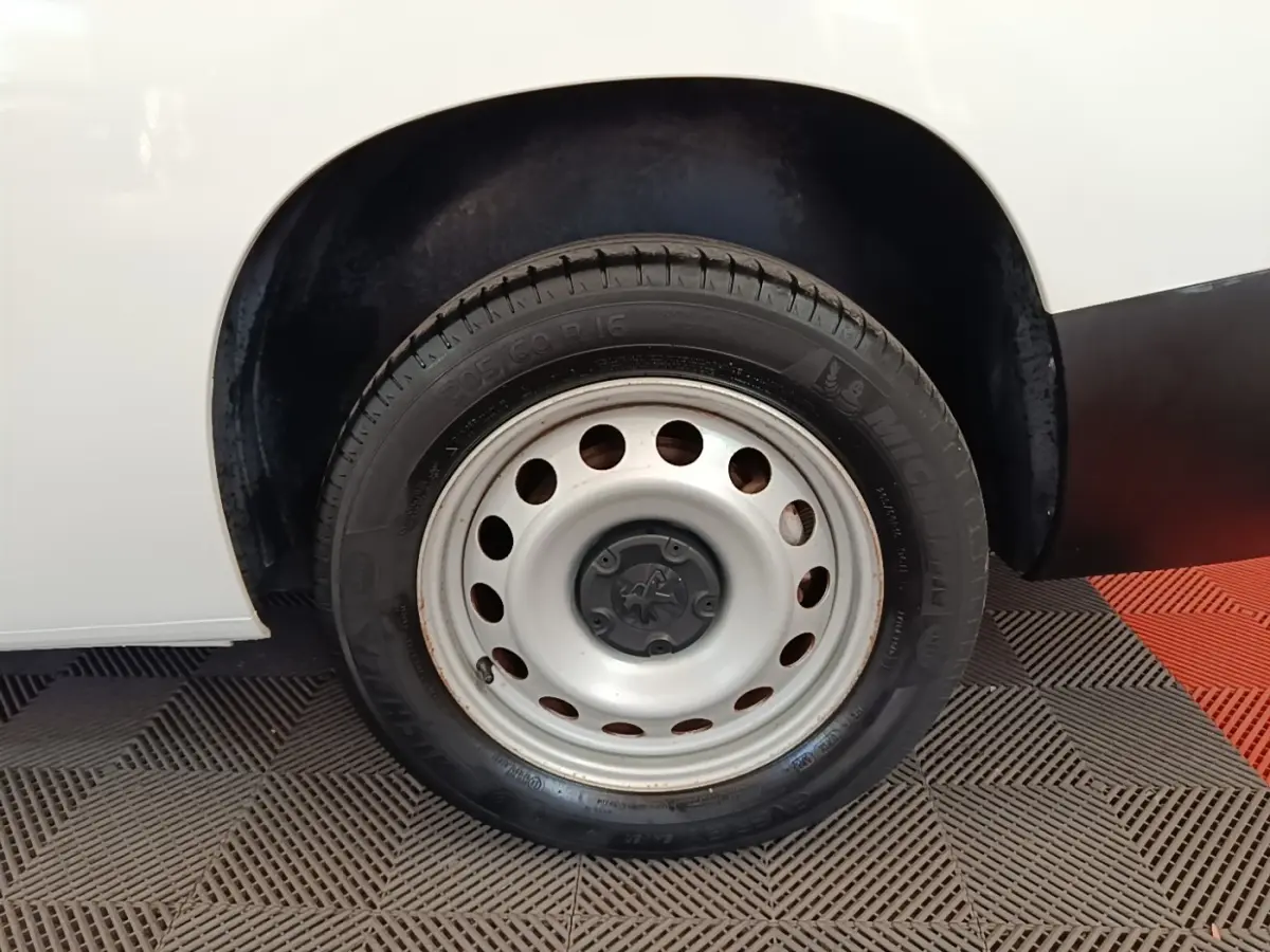 Gros plan sur la roue avant droite en jante acier du Peugeot Partner blanc, avec partie de la carrosserie visible.