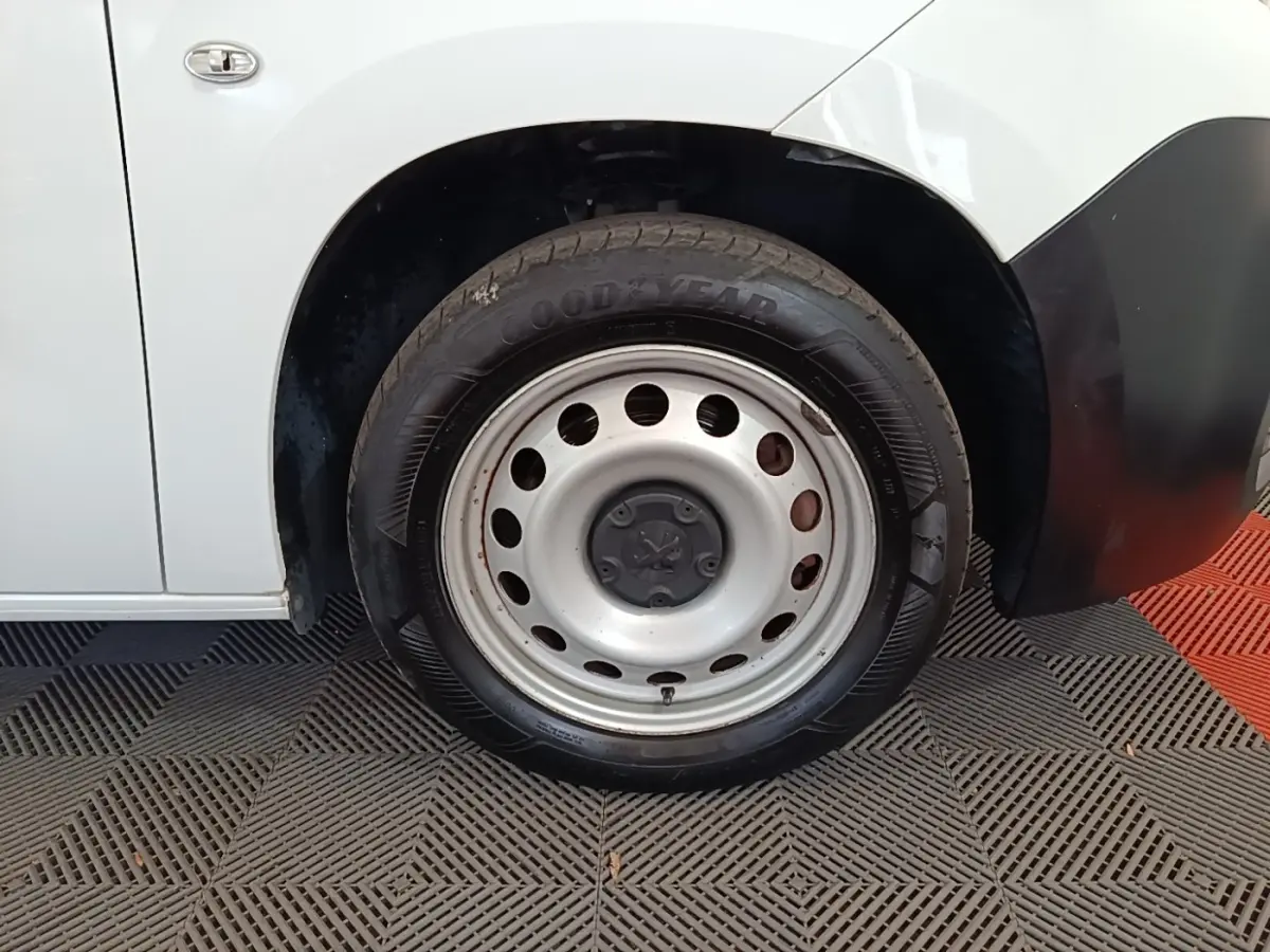 Gros plan sur la roue avant gauche d’un Peugeot Partner blanc avec jante acier et pneu Goodyear.