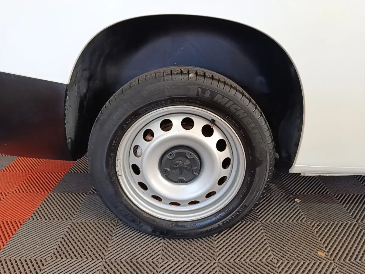 Gros plan sur la roue arrière droite en jante acier du Peugeot Partner blanc, avec logo Peugeot au centre.