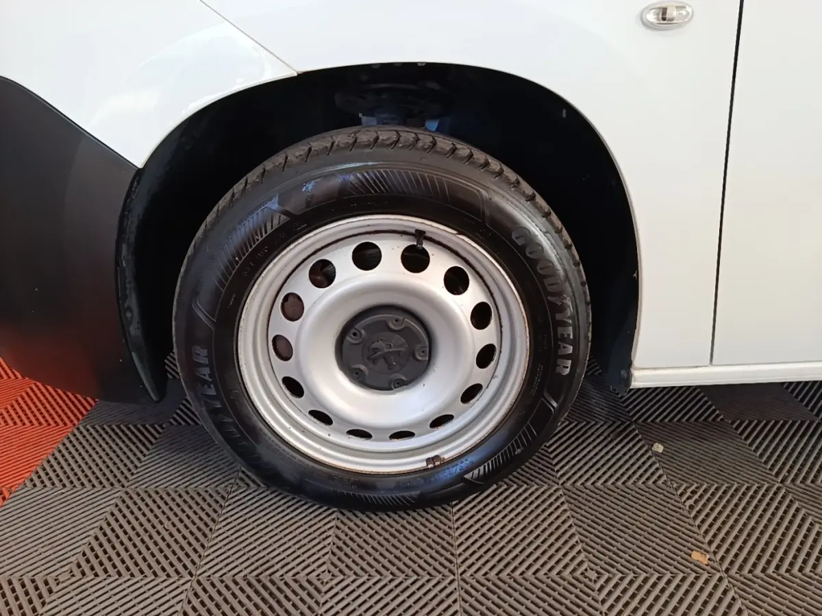 Gros plan sur la roue avant droite en jante acier du Peugeot Partner blanc, avec partie basse de la carrosserie visible.
