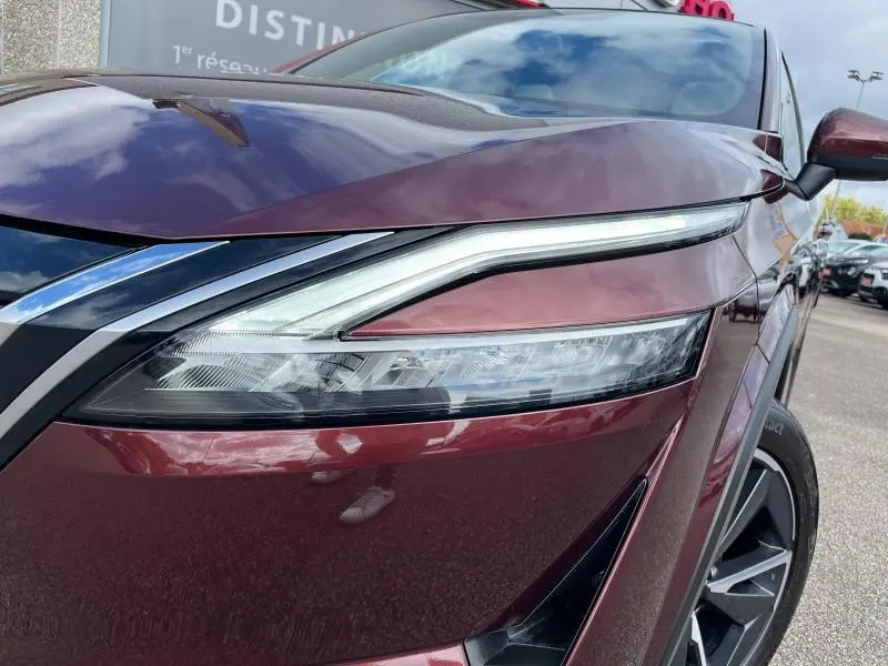Gros plan sur le phare avant gauche du Nissan Qashqai e-POWER 2023 Rouge Passion avec jante alliage 19 pouces visible.