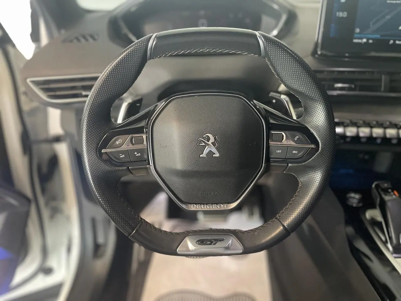 Gros plan sur le volant cuir perforé noir du Peugeot 3008 GT avec logo lion et badge GT en bas.