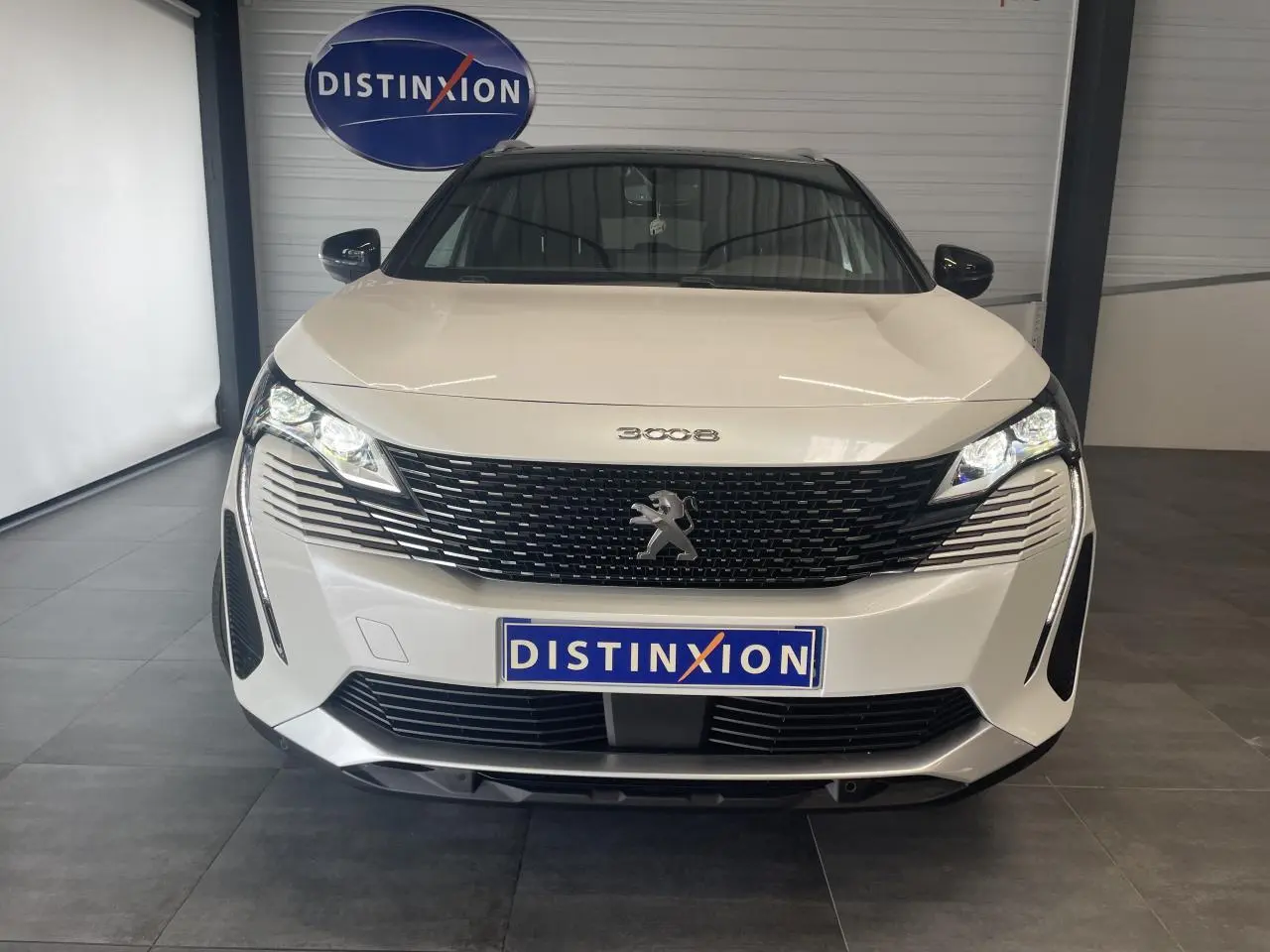 Vue avant d'un Peugeot 3008 blanc nacré avec calandre noire et logo lion chromé, en intérieur showroom.