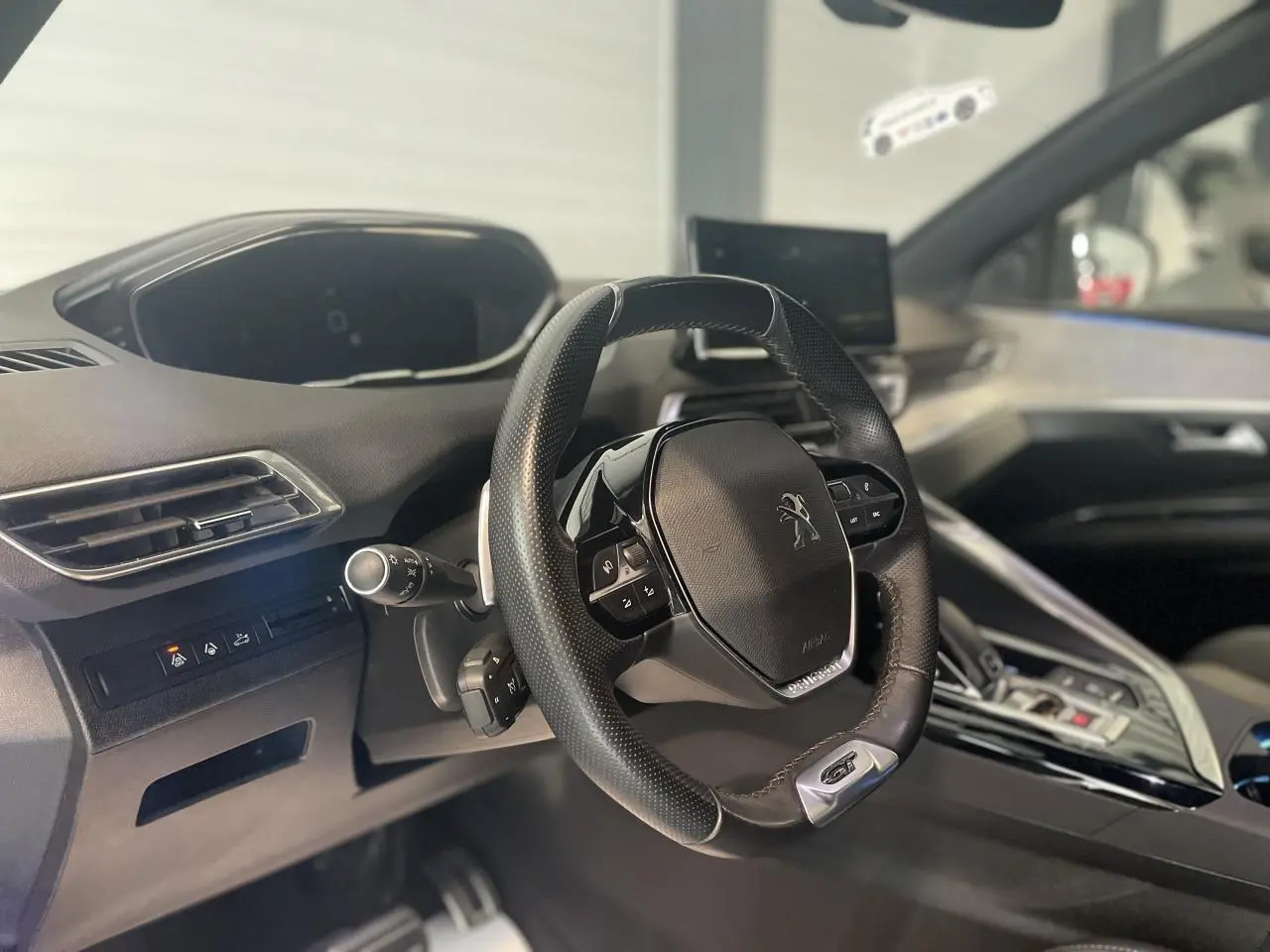 Vue intérieure centrée sur le volant GT cuir perforé et tableau de bord du Peugeot 3008 blanc nacré 2022.