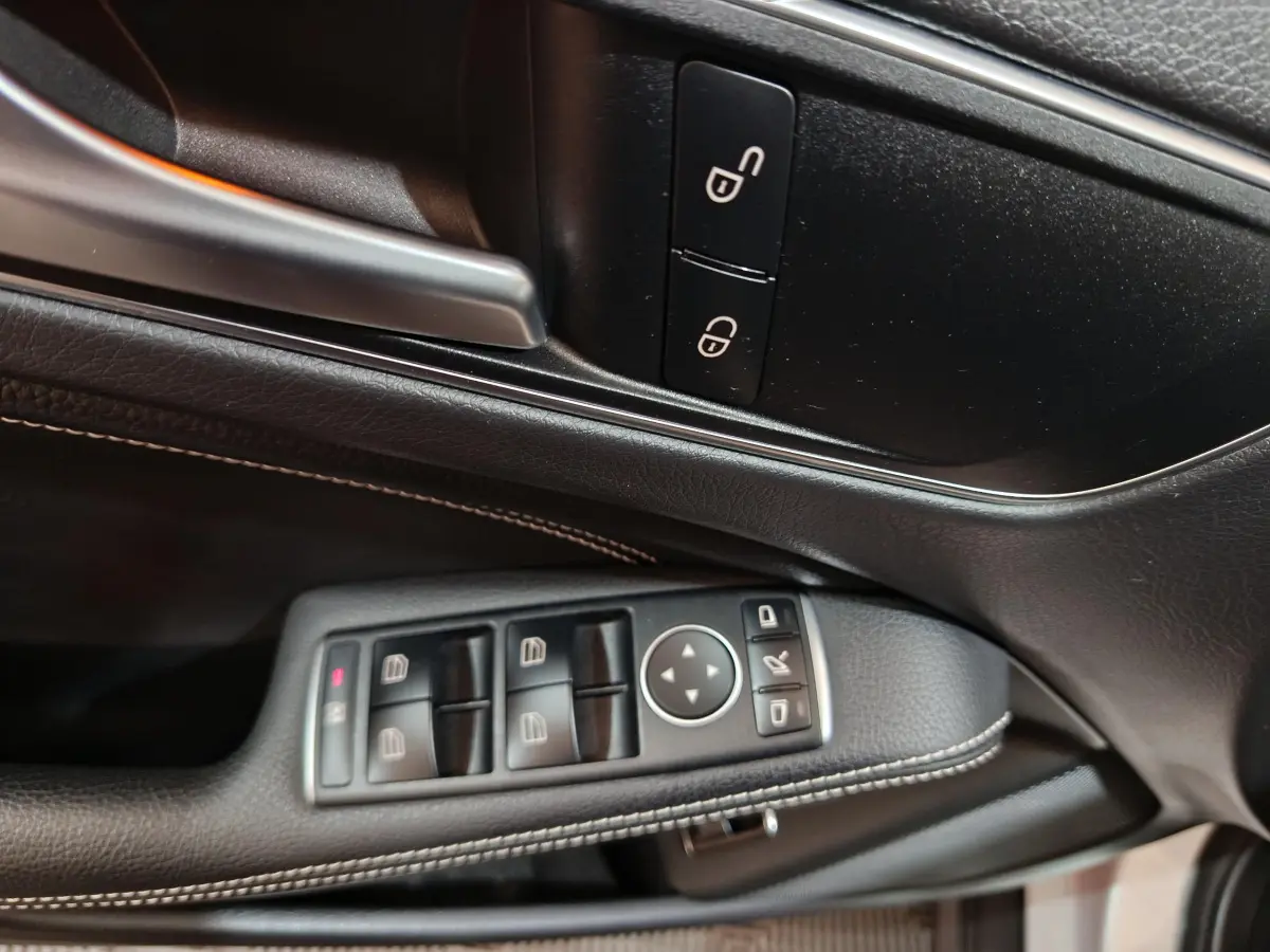 Gros plan sur la commande des vitres et rétroviseurs côté gauche en cuir noir avec surpiqûres blanches dans une Mercedes GLA 200 d.