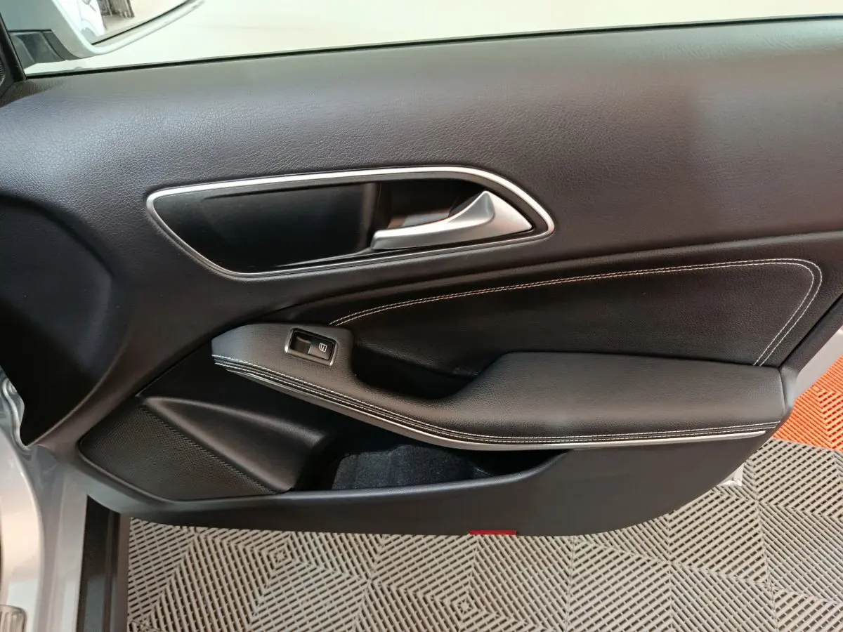 Vue intérieure de la porte côté conducteur d'une Mercedes GLA 200 d gris clair, avec garniture noire et surpiqûres blanches.