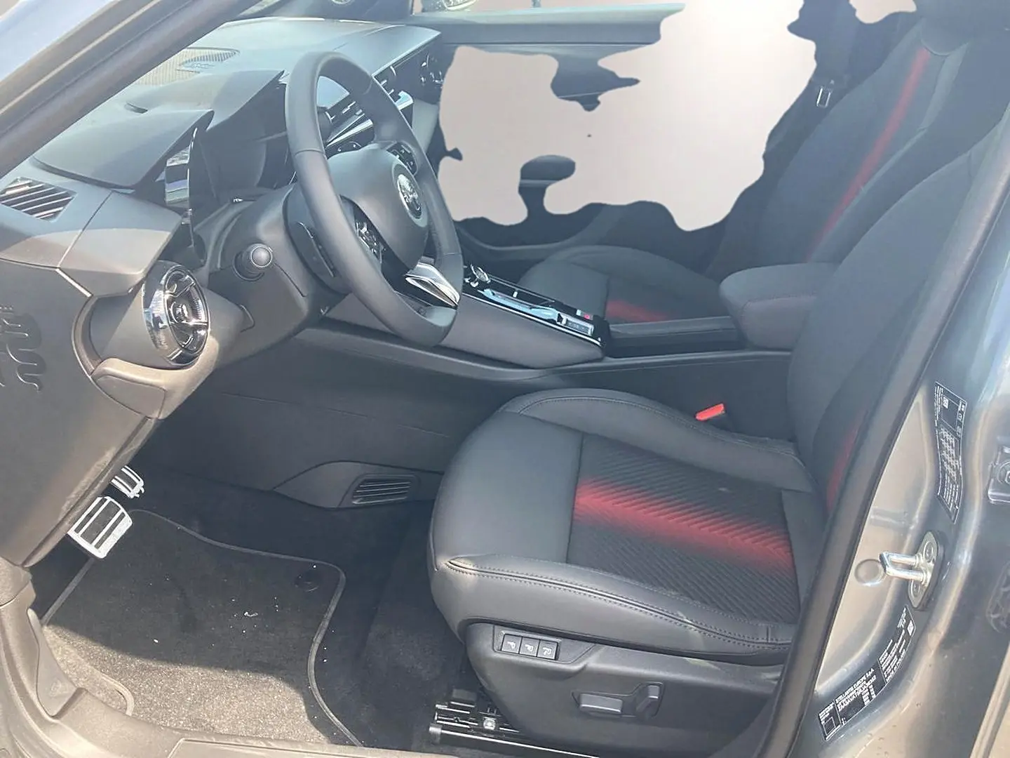 Vue intérieure côté conducteur de l'Alfa Romeo Junior 1.2 hybride grise, sièges noirs avec surpiqûres rouges et volant multifonction.