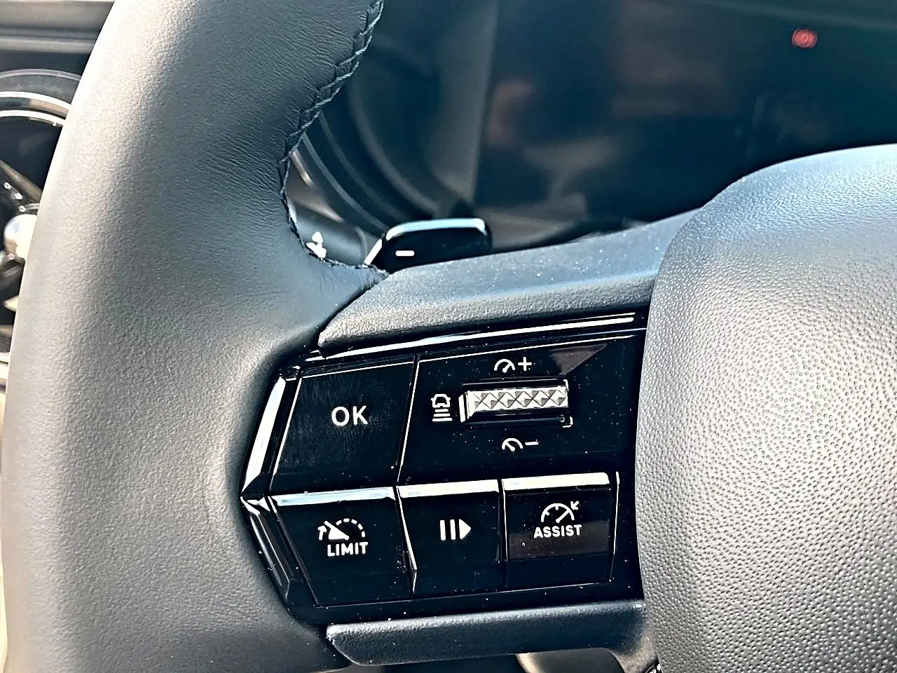 Gros plan sur les commandes noires au volant gris de l'Alfa Romeo Junior 1.2 hybride 2026, avec boutons de régulateur et assistance.