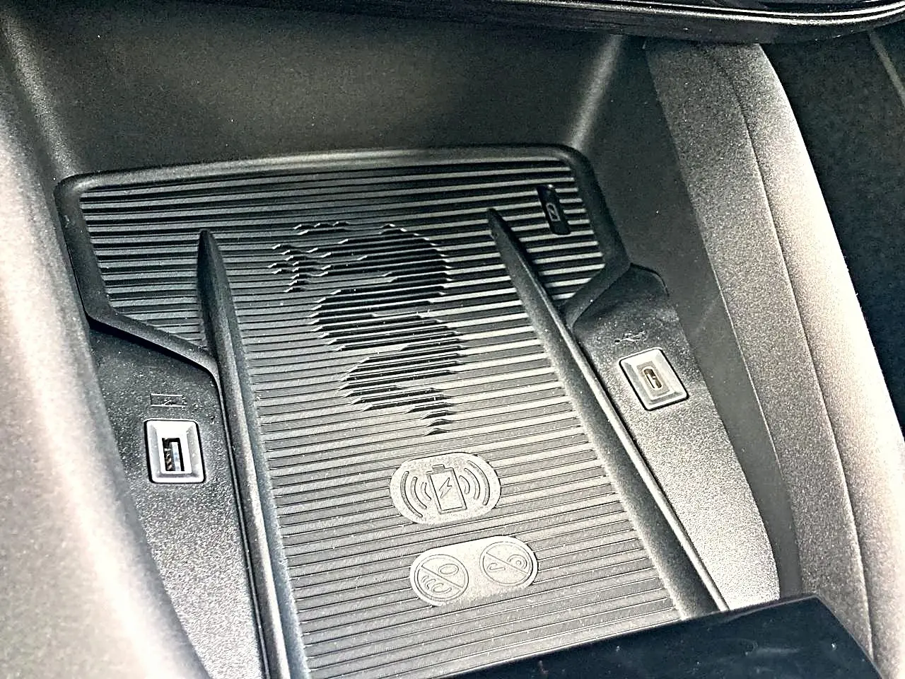 Gros plan sur le chargeur à induction avec logo Alfa Romeo et ports USB dans l’habitacle du Junior gris.