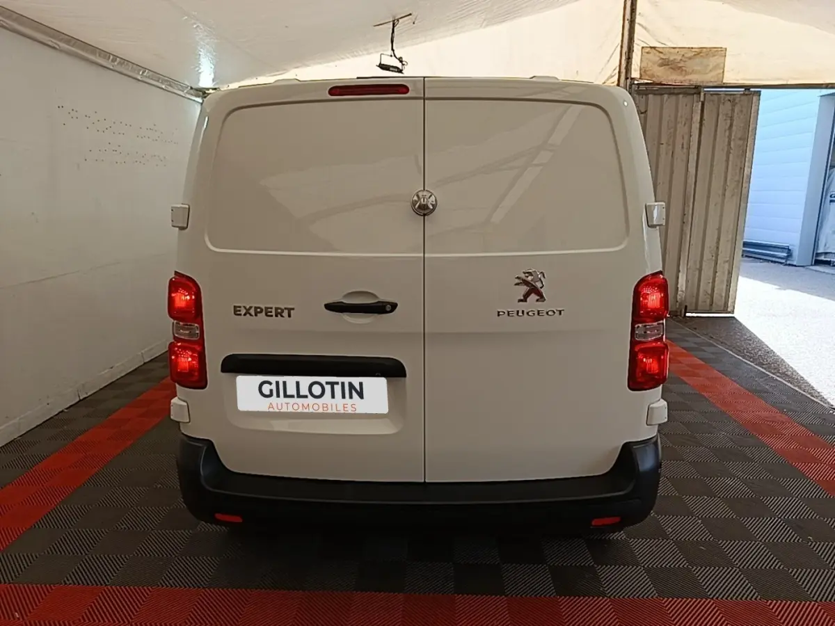 Vue arrière d’un Peugeot Expert Fourgon blanc stationné en intérieur, feux arrière allumés et porte double fermée.