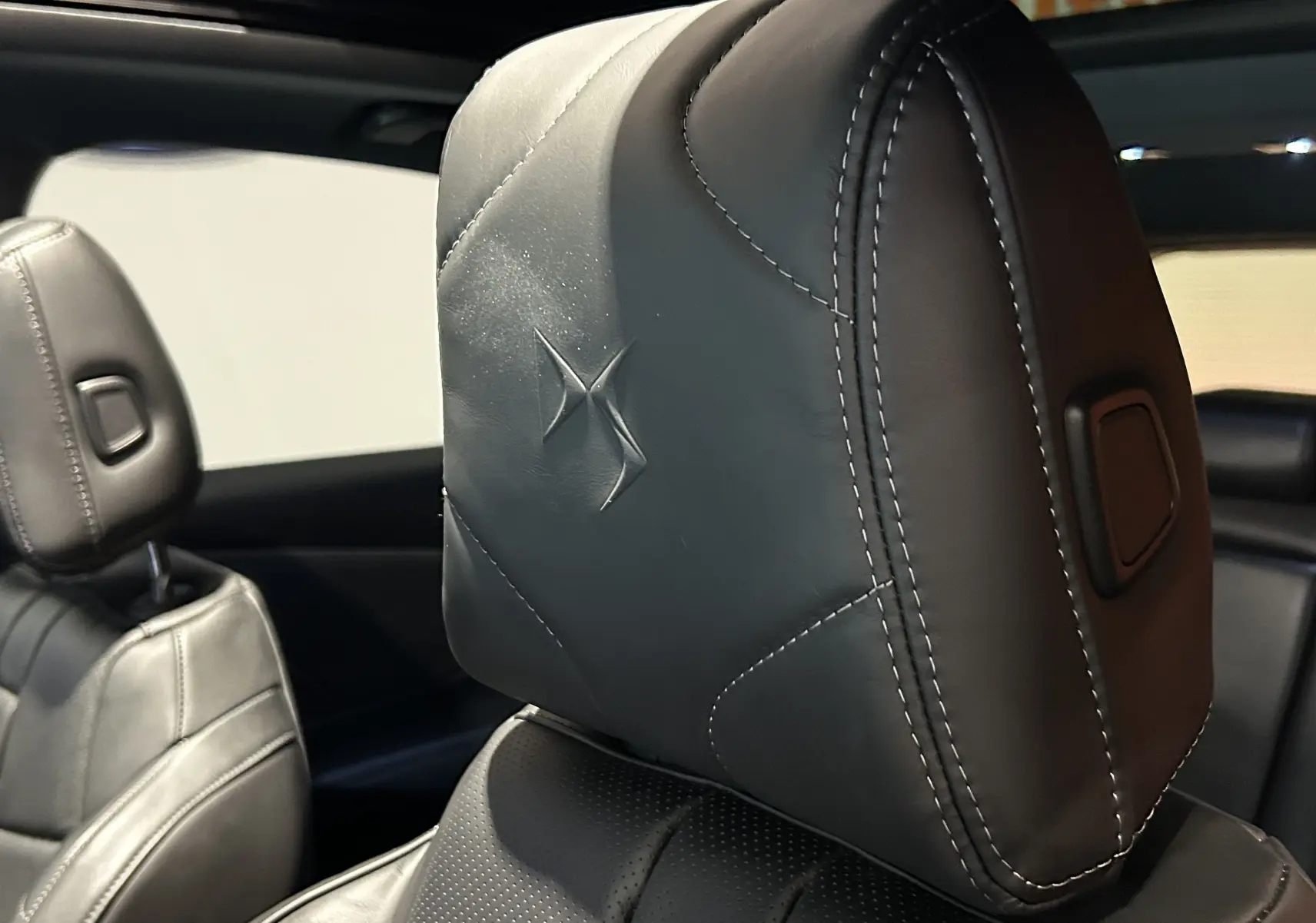 Gros plan sur l'appui-tête en cuir noir embossé du logo DS à l'intérieur du DS7 2024 avec toit ouvrant.