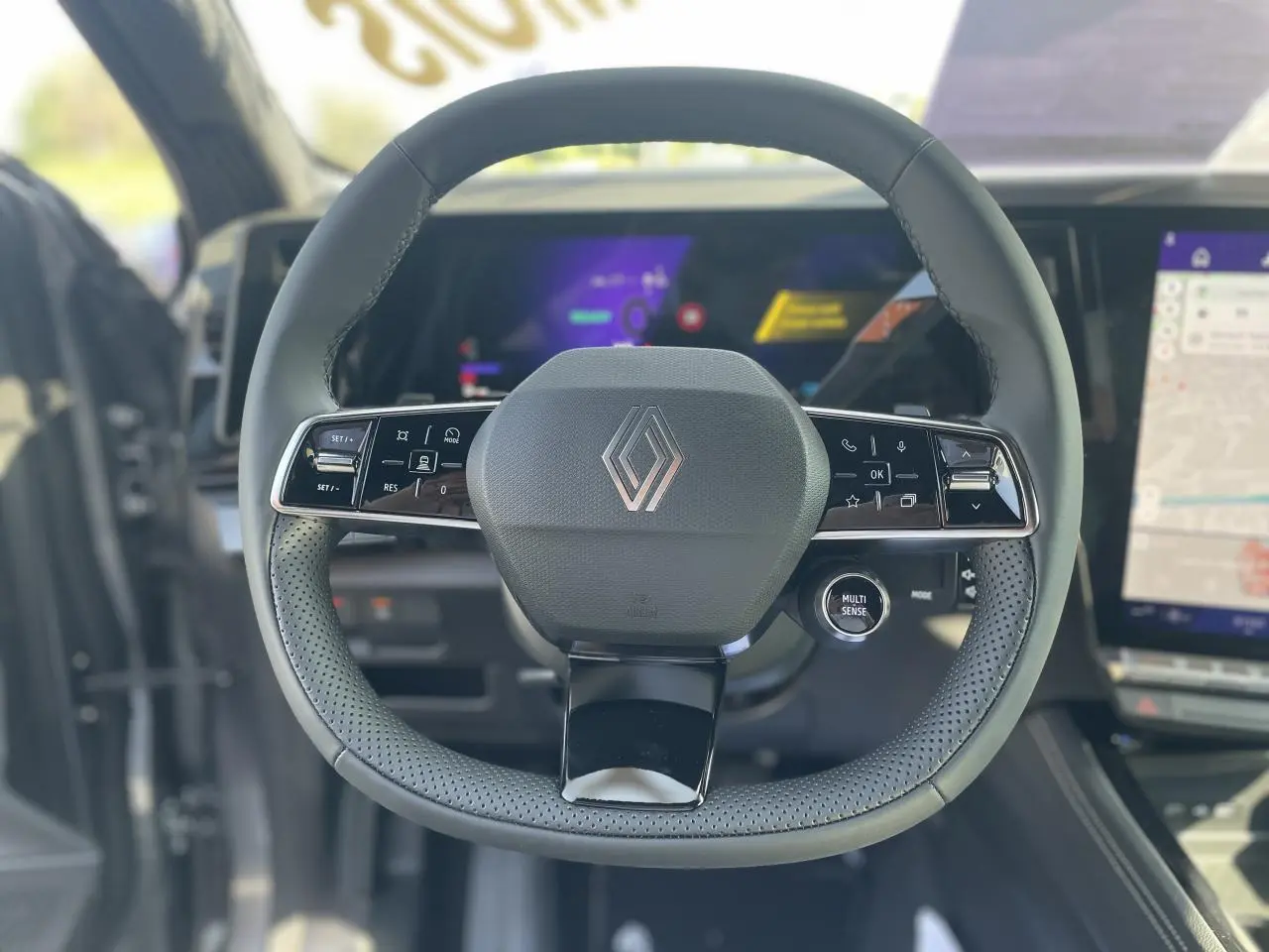 Vue rapprochée du volant noir perforé de la Renault Rafale 2025 avec commandes intégrées et logo central chromé.