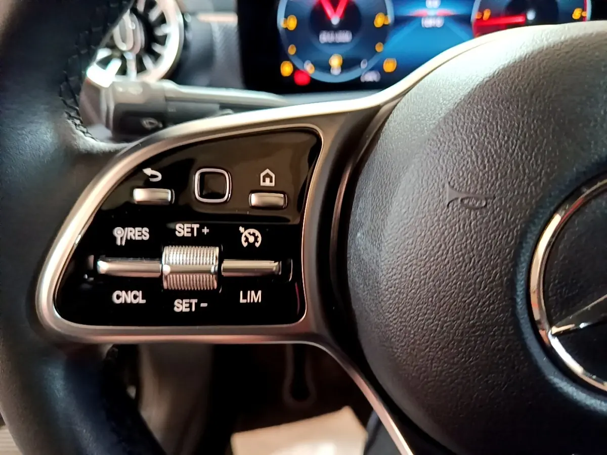 Gros plan sur la partie gauche du volant cuir noir d’une Mercedes Classe A 2022 avec commandes de régulateur de vitesse et affichage numérique en arrière-plan.