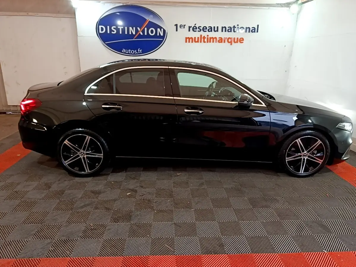 Vue latérale droite d'une Mercedes Classe A Berline noire 2022, avec jantes alliage et vitres teintées, en intérieur showroom.