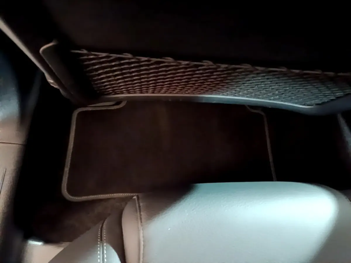 Vue intérieure du coffre arrière d'une Mercedes Classe A berline noire, montrant le tapis de sol et un filet de rangement.