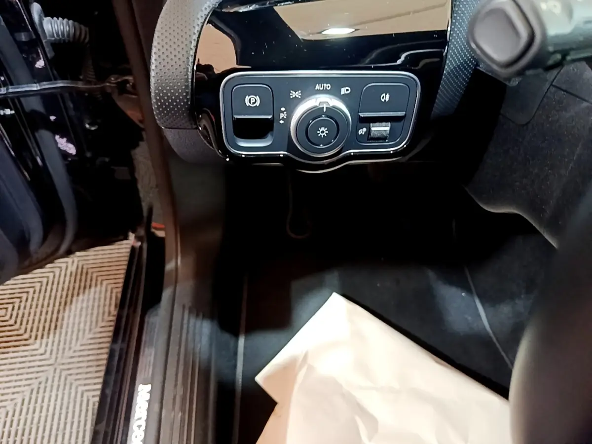 Vue intérieure côté conducteur de la Mercedes Classe A noire, avec commande des feux et frein à main électrique.