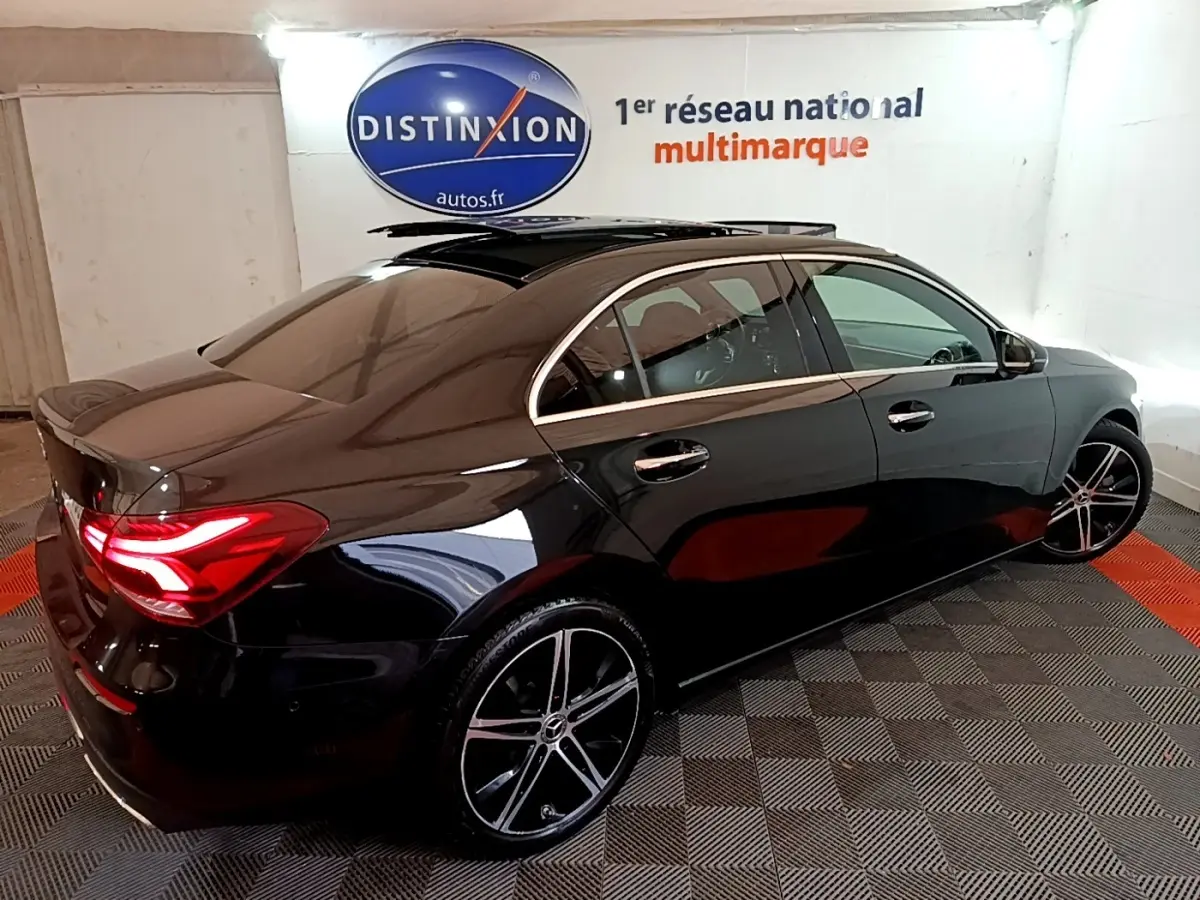 Vue 3/4 arrière droite d'une Mercedes Classe A Berline noire avec feux LED allumés dans un showroom.