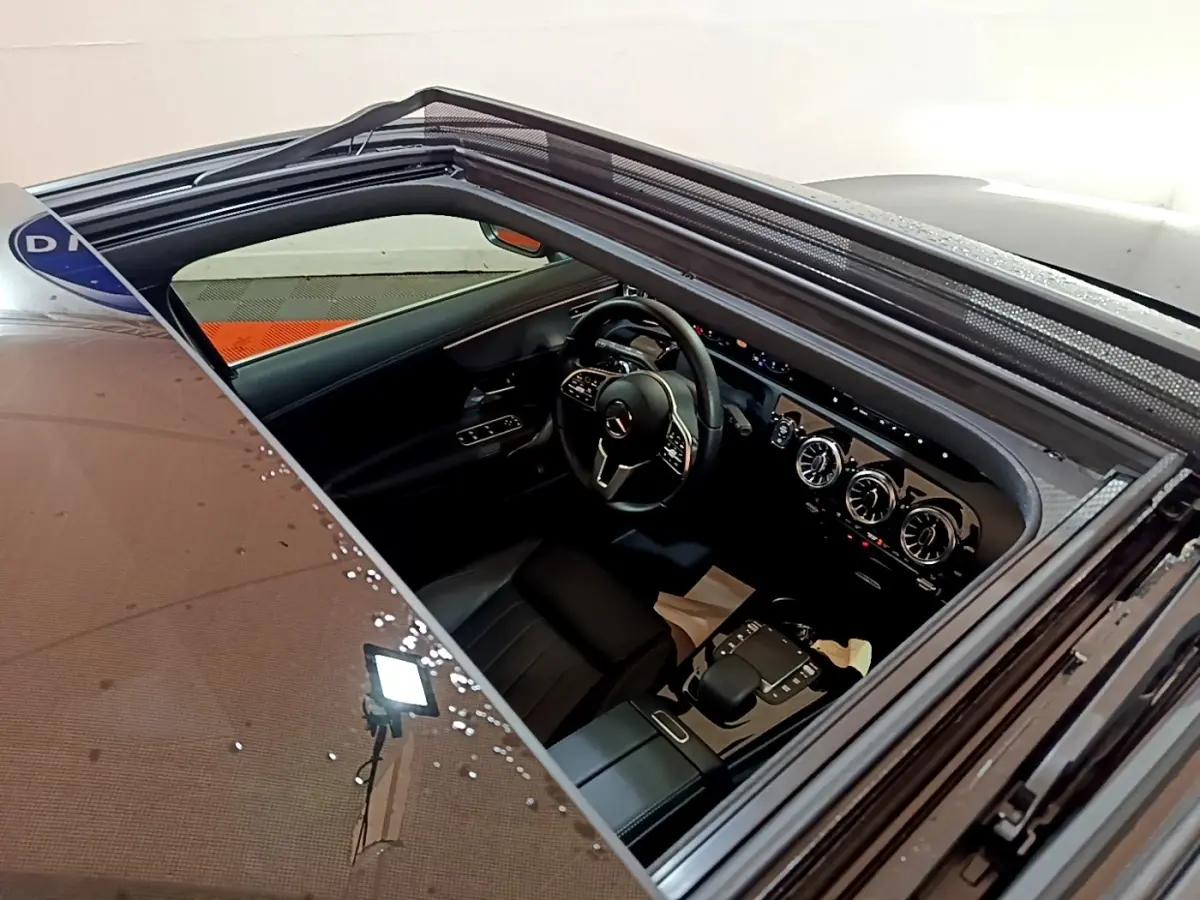 Vue intérieure par le toit ouvrant d'une Mercedes Classe A noire, mettant en valeur le volant cuir et la console centrale moderne.
