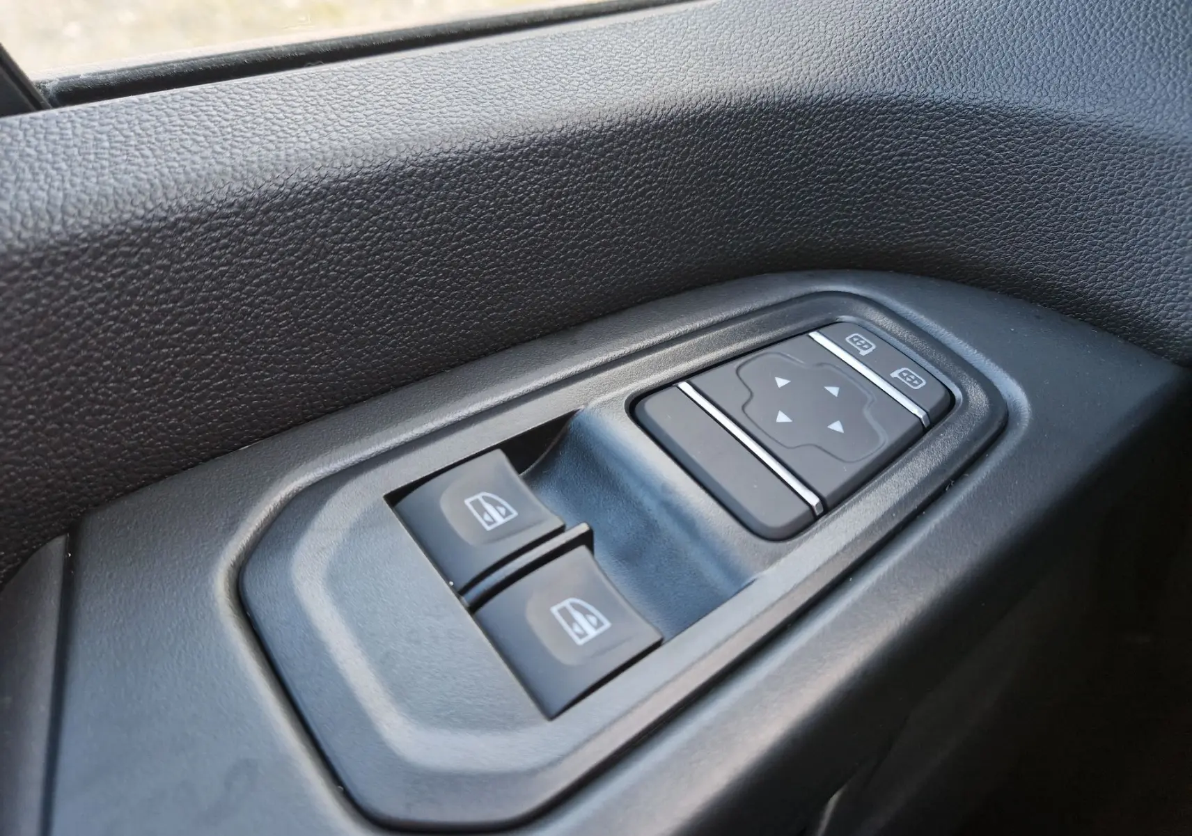 Gros plan sur les commandes de lève-vitres et réglage des rétroviseurs côté conducteur du Renault Trafic Fourgon gris Highland.