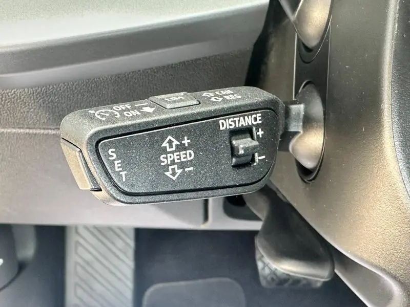 Gros plan sur la commande de régulateur de vitesse adaptatif noir à gauche du volant dans l'Audi A3 Sportback blanc Arkona 2024.