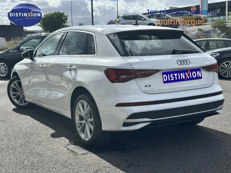 Audi A3 Sportback blanc Arkona vue 3/4 arrière droit, soulignant son design hybride et ses feux arrière LED.