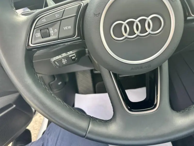 Gros plan sur le volant cuir multifonction noir de l'Audi A3 Sportback 2024 avec commandes intégrées et logo Audi central argenté.