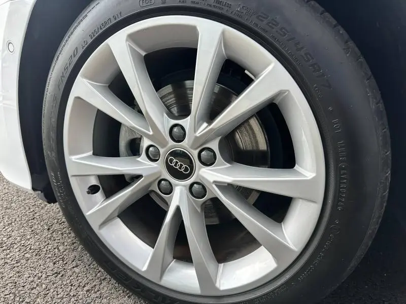 Gros plan sur la jante aluminium argentée de l'Audi A3 Sportback blanc Arkona, avec logo Audi au centre.