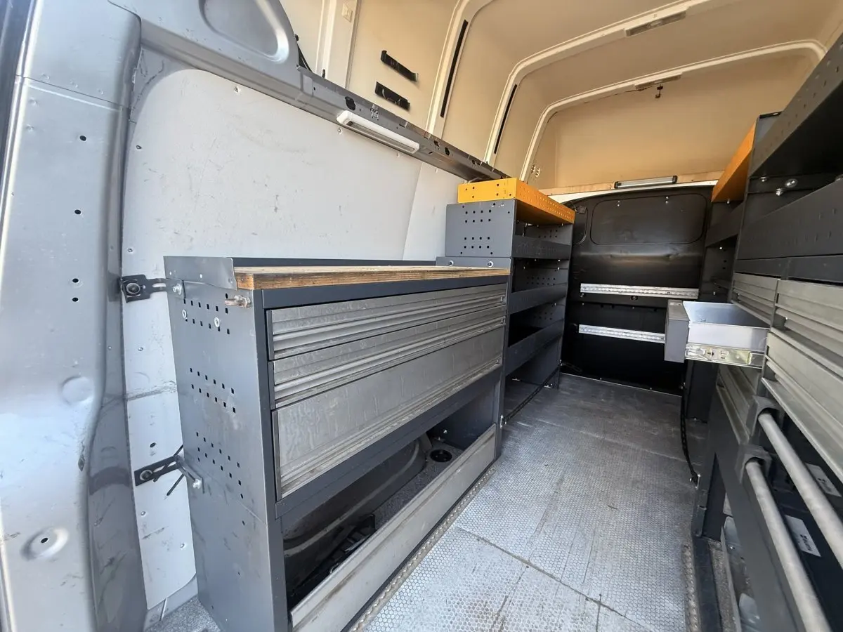Vue intérieure arrière du Volkswagen Transporter gris clair 2022, montrant l'aménagement avec étagères et rangements métalliques.