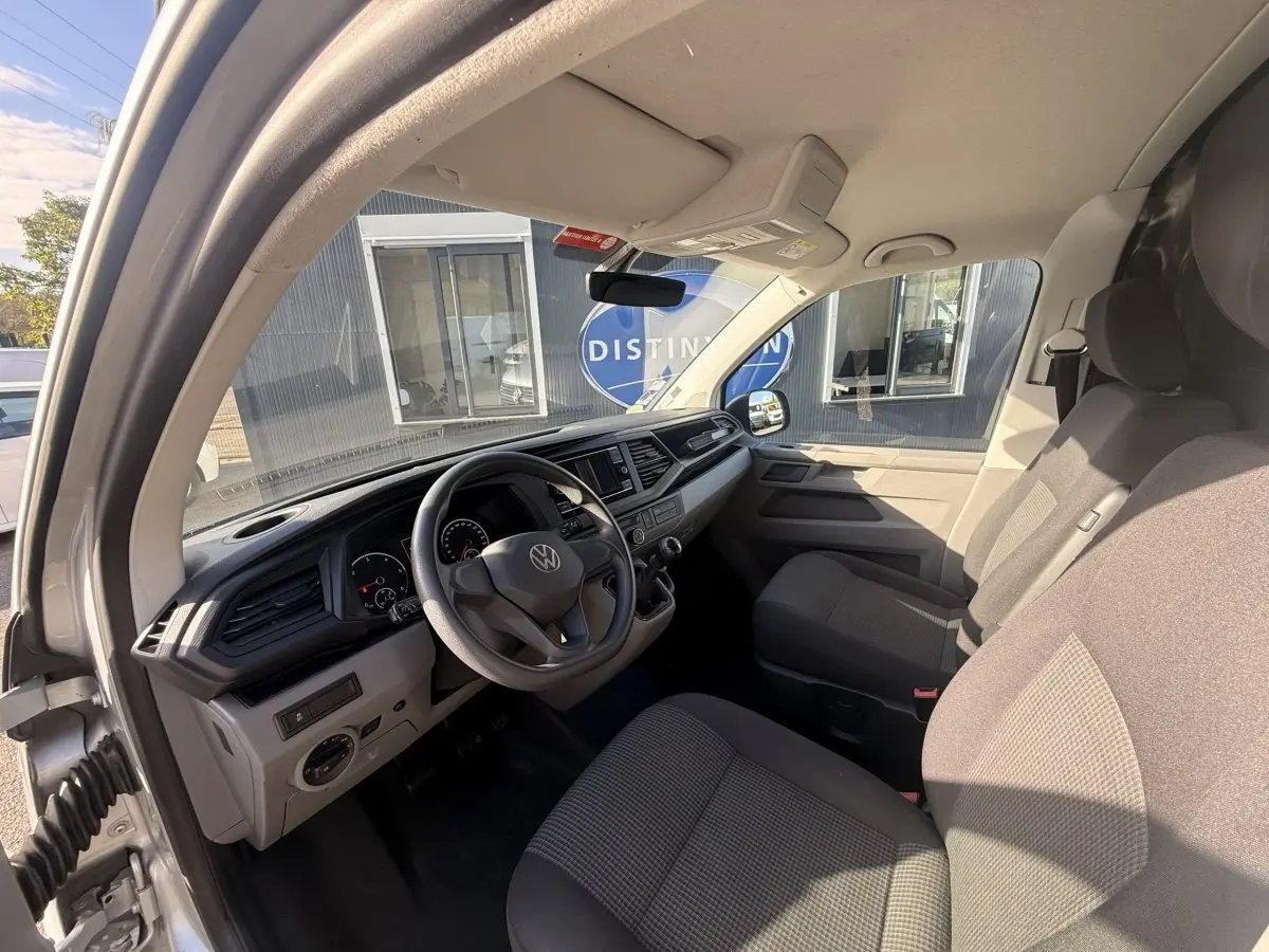 Vue intérieure côté conducteur du Volkswagen Transporter gris clair 2022, montrant le tableau de bord et les sièges avant.