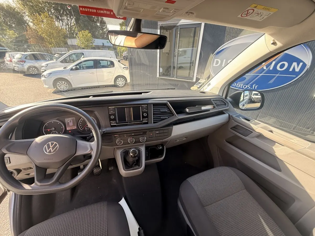 Vue intérieure avant du Volkswagen Transporter gris clair 2022, tableau de bord avec écran tactile et volant manuel.