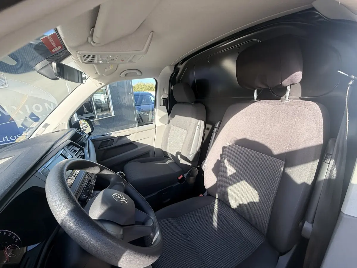 Vue intérieure côté conducteur du Volkswagen Transporter gris clair 2022, montrant le volant et les sièges avant en tissu.