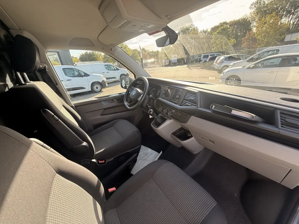 Vue intérieure côté conducteur du Volkswagen Transporter gris clair 2022, tableau de bord et sièges avant visibles.