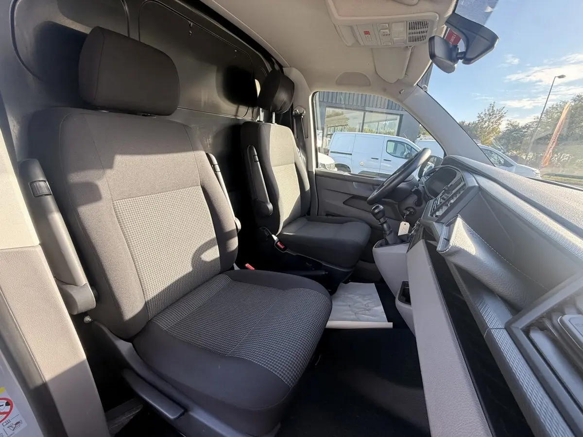 Vue intérieure côté conducteur du Volkswagen Transporter gris clair 2022, montrant les sièges avant et le tableau de bord.