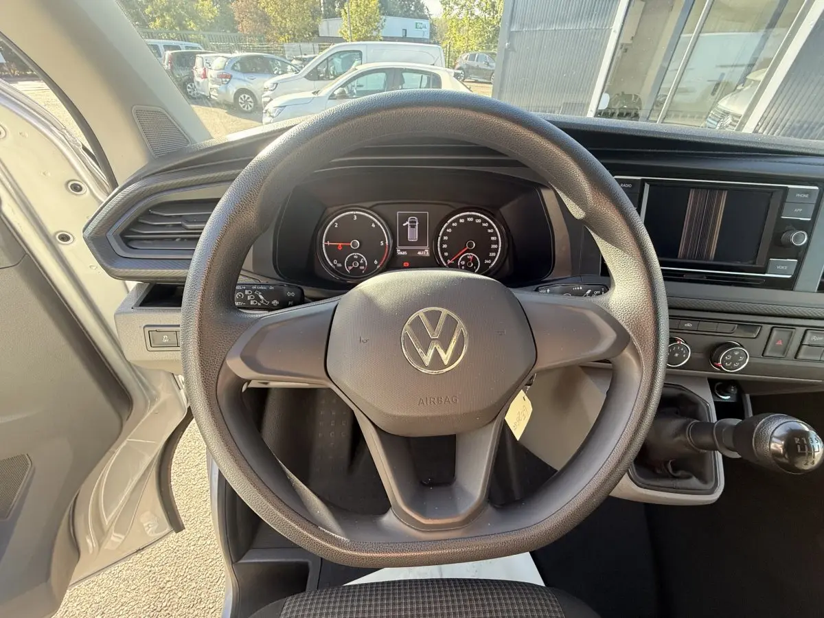 Vue intérieure centrée sur le volant noir et le tableau de bord du Volkswagen Transporter gris clair, avec levier de vitesses manuel visible.