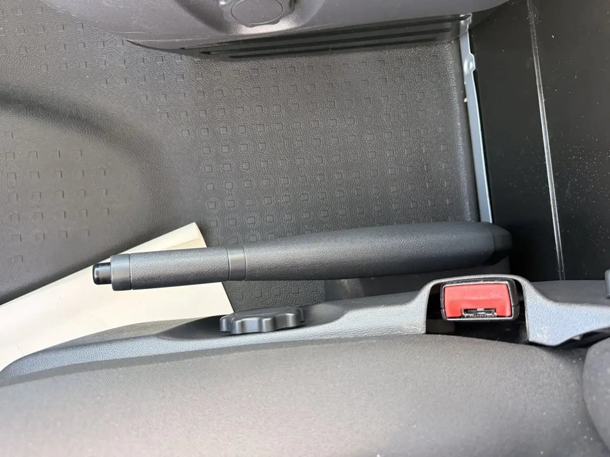 Vue rapprochée de la poignée de frein à main noire et de la ceinture de sécurité rouge dans un Volkswagen Transporter gris clair.