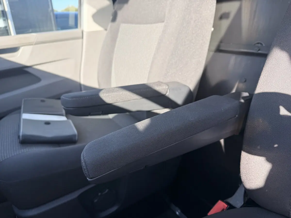 Gros plan sur les accoudoirs noirs des sièges avant d’un Volkswagen Transporter gris clair, intérieur lumineux.