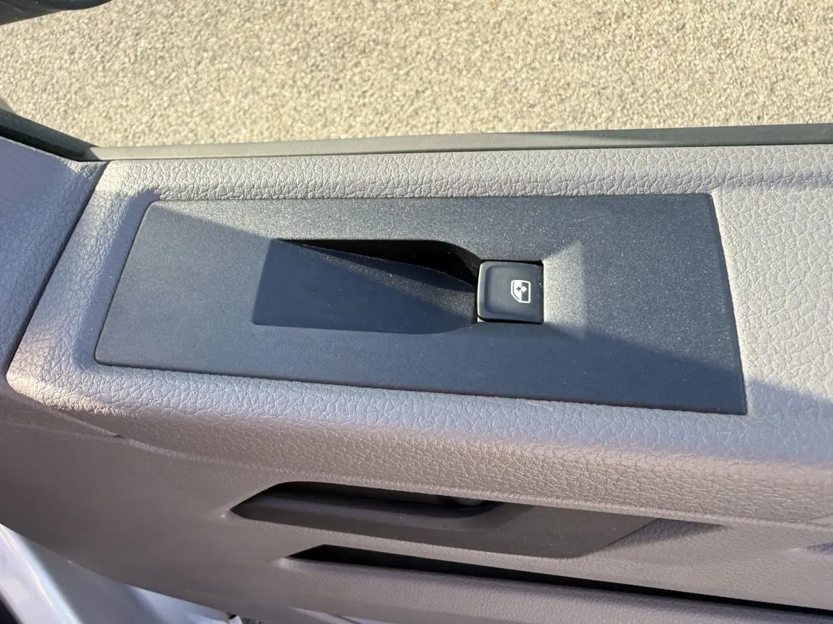 Gros plan sur le bouton de commande de la vitre électrique côté conducteur d’un Volkswagen Transporter gris clair 2022.