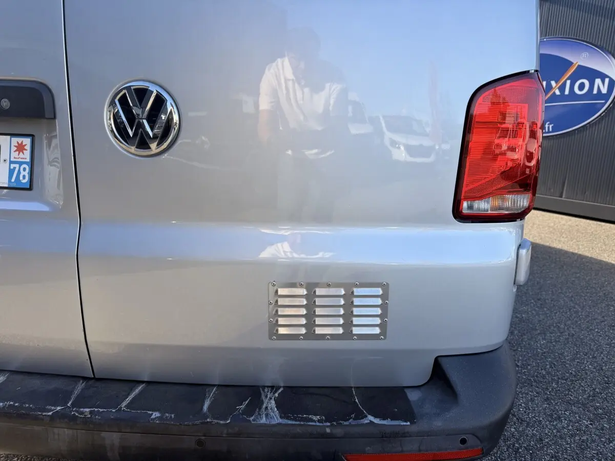 Vue arrière droite du Volkswagen Transporter gris clair avec feu arrière rouge et logo VW visible sur la porte.