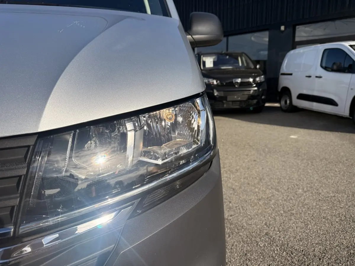 Gros plan sur le phare avant gauche du Volkswagen Transporter gris clair, avec calandre noire visible.