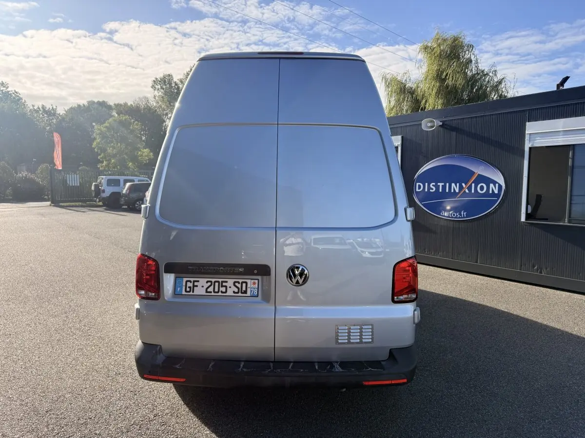 Vue arrière d’un Volkswagen Transporter gris clair 2.0 TDi 110 L2H1 avec portes battantes fermées, stationné en extérieur.